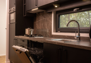 Cocina moderna en una cabaña con estufa de gas, fregadero, lavavajillas y ventana con vistas al bosque.