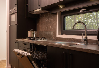 Cocina moderna en una cabaña con estufa de gas, fregadero, lavavajillas y ventana con vistas al bosque.