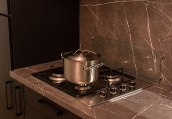 Photo de cuisine montrant une casserole en inox avec couvercle sur une cuisinière à gaz et un plan de travail en marbre dans un lodge.