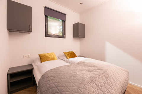Chambre de lodge avec deux lits simples, coussins dorés, couvre-lit gris et armoires modernes.
