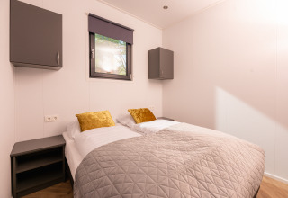 Lodge slaapkamer met twee enkele bedden, gouden kussens, grijs dekbed en moderne wandkasten.
