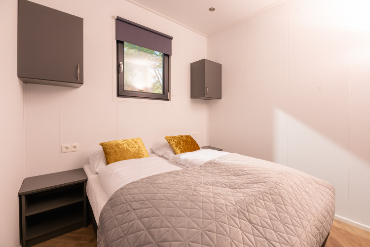Lodge bedroom with two single beds, gold pillows, a grey quilt, and modern wall-mounted cabinets.