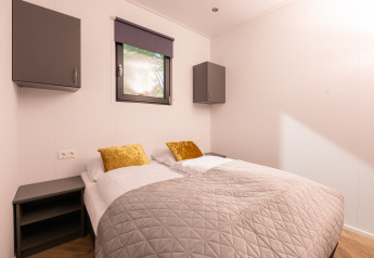 Lodge slaapkamer met twee eenpersoonsbedden, gouden kussens, grijs dekbed en moderne kasten.