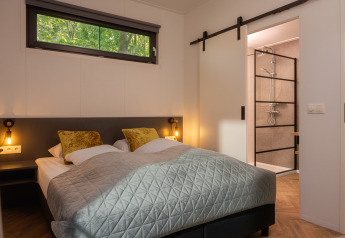 Dormitorio moderno en una cabaña con cama doble, cojines dorados y baño accesible con ducha.