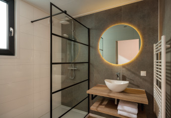 Modernes Lodge-Badezimmer mit Regendusche, beleuchtetem rundem Spiegel, Holzwaschtisch und Handtüchern.