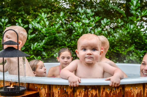 Varios niños disfrutan de un jacuzzi al aire libre junto a una tiny house, rodeados de vegetación y una linterna.