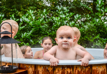 Meerdere kinderen genieten van een warm bubbelbad buiten bij een tiny house, omringd door groen en een lantaarn.
