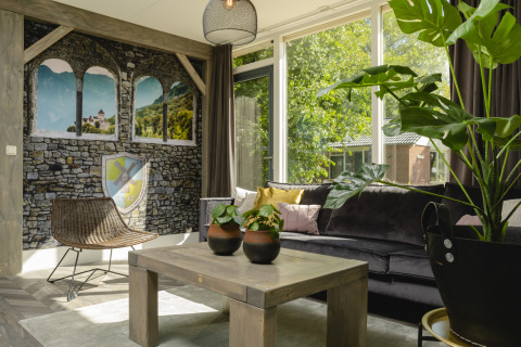 Lyst og hyggeligt opholdsrum i en familiebungalow med plantepynt, vægmaleri og store vinduer i Holiday Park Mölke.