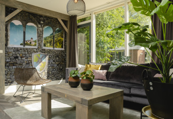 Lyst og hyggeligt opholdsrum i en familiebungalow med plantepynt, vægmaleri og store vinduer i Holiday Park Mölke.