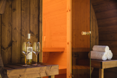 Une bouteille de vin et deux verres sur une table en bois devant un sauna au Luxury lodge + sauna du Vakantiepark Hölte.