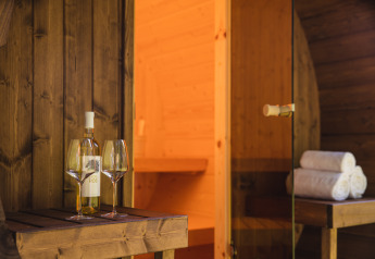 Eine Weinflasche und zwei Gläser stehen auf einem Holztisch vor einer Sauna im Vakantiepark Hölte.