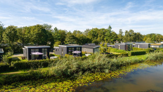 Kleine huisjes aan een met waterlelies bezaaide rivier, groen omgeven, genaamd River Cabin met hot tub.