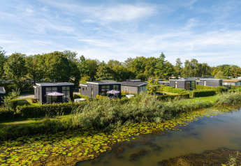 Kleine huisjes aan een met waterlelies bezaaide rivier, groen omgeven, genaamd River Cabin met hot tub.