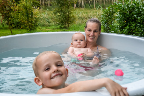 Mutter und zwei Kinder entspannen im Whirlpool vor der River Cabin im Holiday Park Mölke, Niederlande.