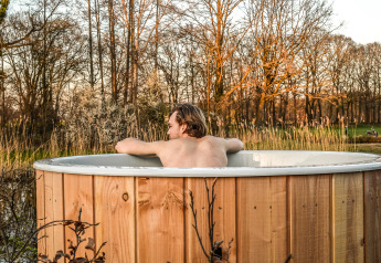 Persoon ontspant in een houten hottub aan het water bij River Cabin in Vakantiepark Mölke, Nederland.
