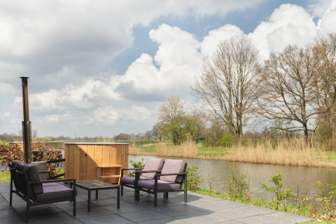 Terrasse avec fauteuils, petite table et bain à remous au bord de la rivière au Holiday Park Mölke, Pays-Bas.