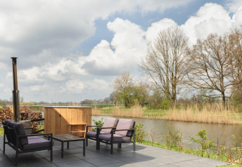 Terras met comfortabele zitjes, tafeltje en hottub aan de rivier bij Holiday Park Mölke, Nederland.