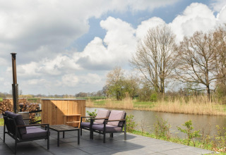 Terrasse avec fauteuils, petite table et bain à remous au bord de la rivière au Holiday Park Mölke, Pays-Bas.