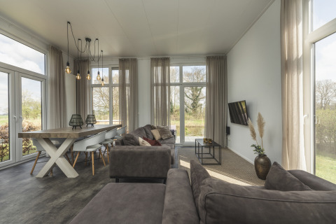 Modern, bright living room in a tiny house at Holiday Park Mölke with large windows and a grey sofa.
