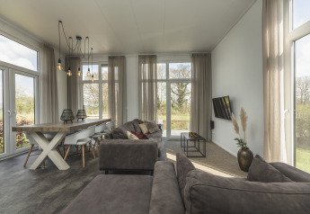 Moderne, lichte woonkamer in een tiny house bij Holiday Park Mölke met grote ramen en grijze zetel.