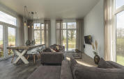 Moderne, lichte woonkamer in een tiny house bij Holiday Park Mölke met grote ramen en grijze zetel.