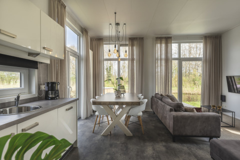 Interior de tiny house moderno en River Cabin, Holiday Park Mölke, con cocina, mesa y ventanales grandes.