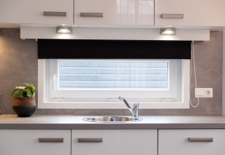 Modern kitchen sink beneath a window with a roller blind in a tiny house at Holiday Park Mölke, Netherlands.