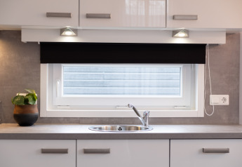 Modern kitchen sink beneath a window with a roller blind in a tiny house at Holiday Park Mölke, Netherlands.