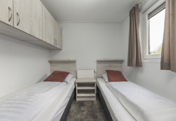 Moderne glamping-accommodatie met twee eenpersoonsbedden, bruine kussens, kasten en een raam met gordijnen.