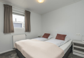 Lichte glamping slaapkamer met een tweepersoonsbed, nachtkastjes, raam met gordijnen en radiator.