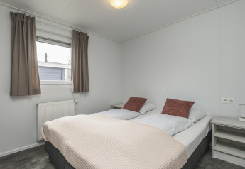 Lichte glamping slaapkamer met tweepersoonsbed, nachtkastjes, raam met gordijnen en radiator.