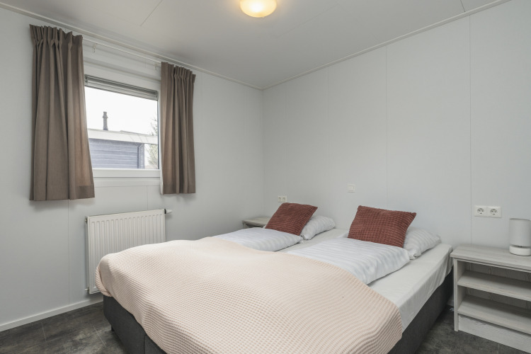 Habitación glamping luminosa con cama doble, mesitas de noche, ventana con cortinas y radiador.