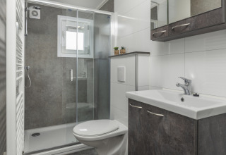 Modern glamping bathroom with wall-mounted toilet, glass shower enclosure, and sleek sink unit.