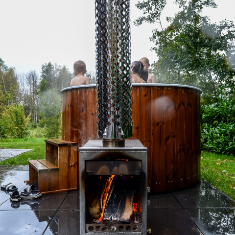 Holzbefeuerter Whirlpool draußen bei der River Cabin im Holiday Park Mölke mit Menschen im warmen Wasser.