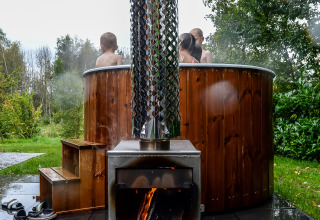 Vasca idromassaggio esterna con stufa a legna al River Cabin di Holiday Park Mölke, Paesi Bassi, con persone.