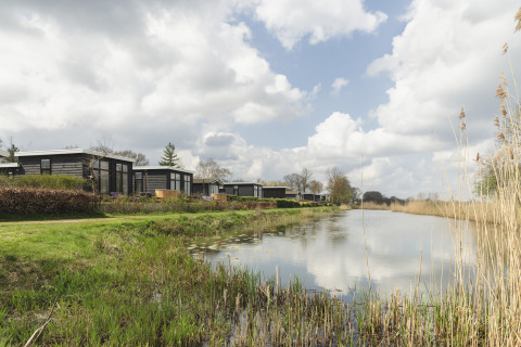 Moderne Tiny Houses am Flussufer mit spiegelndem Wasser und bewölktem Himmel im Ferienpark Mölke.