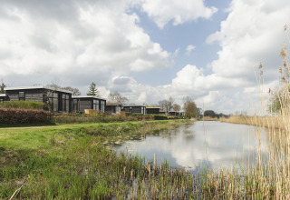 Moderne Tiny Houses am Flussufer mit spiegelndem Wasser und bewölktem Himmel im Ferienpark Mölke.