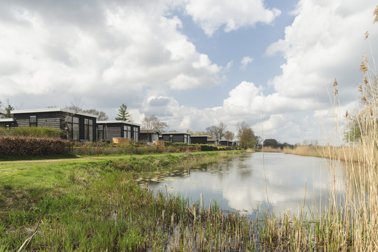 Cabañas modernas junto al río reflejadas en el agua, bajo un cielo parcialmente nublado en Holanda.