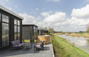 Terrazza del River Cabin con arredo da esterno viola, vasca idromassaggio in legno e vista sul fiume.