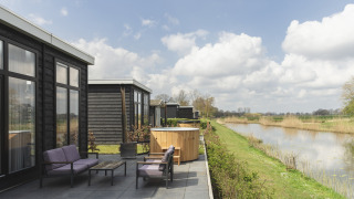 Patio at River Cabin with purple garden furniture, wooden hot tub and riverside view under a blue sky.