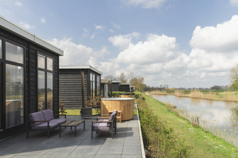 Terrasse du River Cabin avec salon de jardin violet, bain nordique et vue paisible sur la rivière et la nature.