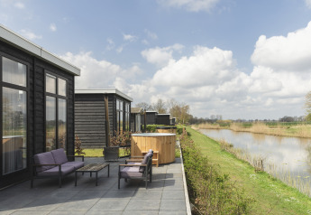 Terrasse der River Cabin mit lila Sitzmöbeln, Whirlpool und Blick auf den Fluss und die grüne Landschaft.