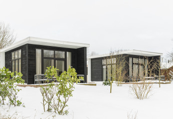 Dos pequeñas casas negras modernas en la nieve en Holiday Park Mölke en los Países Bajos con grandes ventanas.