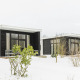 Dos pequeñas casas negras modernas en la nieve en Holiday Park Mölke en los Países Bajos con grandes ventanas.