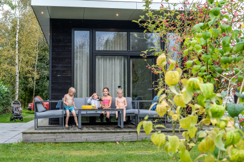 Børn hygger sig på terrassen foran en lille River Cabin med store vinduer i Holiday Park Mölke, Holland.