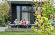 Kids relax on the patio in front of a River Cabin with large windows at Holiday Park Mölke, Netherlands.
