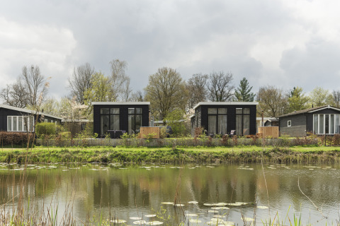To sorte tiny houses med store vinduer og terrasse ved en sø med åkander i Holiday Park Mölke, Holland.