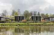 Twee moderne tiny houses aan het water met terras bij Holiday Park Mölke in Nederland in groene omgeving.