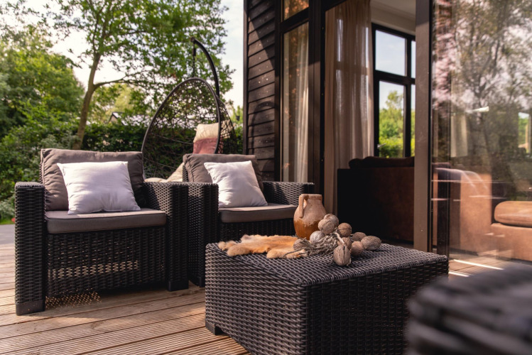 Buiten terras van River Cabin met vlechtmeubilair en kussens bij Holiday Park Mölke, Nederland.