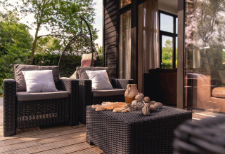 Buiten terras van River Cabin met vlechtmeubilair en kussens bij Holiday Park Mölke, Nederland.